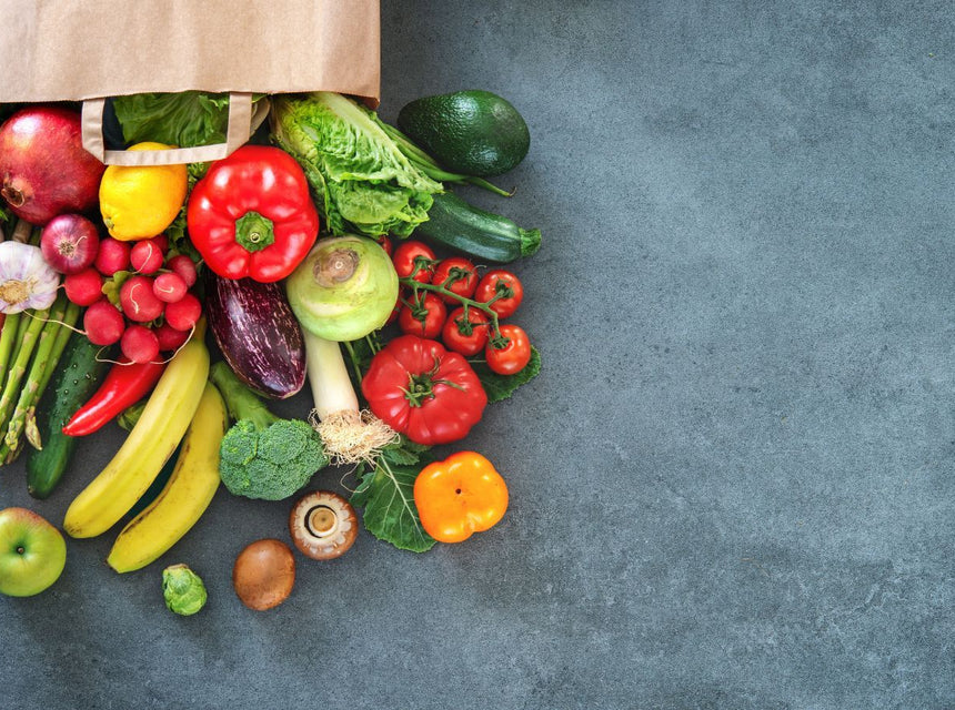 Fresh assortment of high fiber fruits and vegetables spilling from a paper grocery bag.