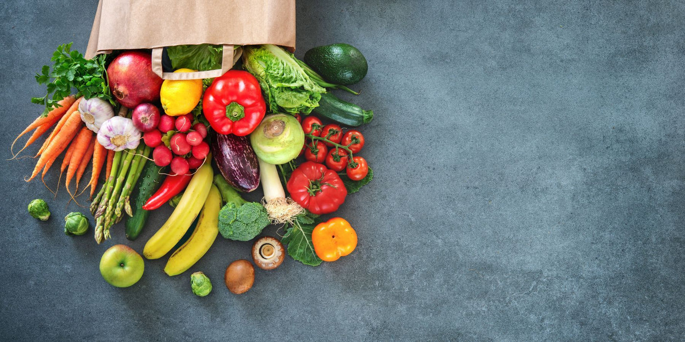 Fresh assortment of high fiber fruits and vegetables spilling from a paper grocery bag.