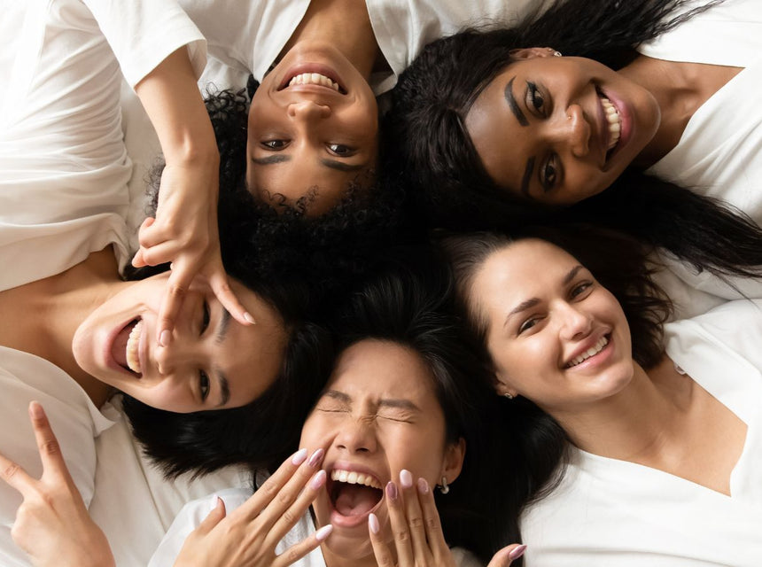 Group of women lying on a bed in white tops smiling together