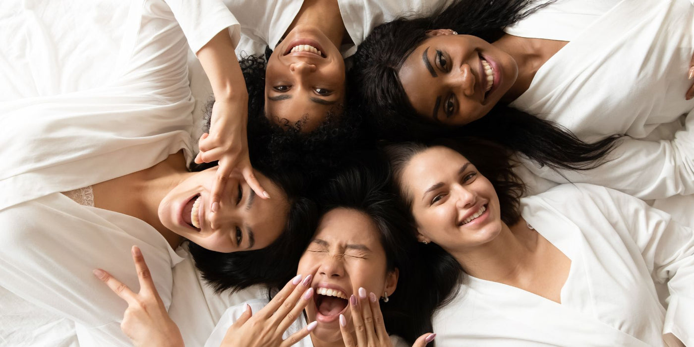 Group of women lying on a bed in white tops smiling together
