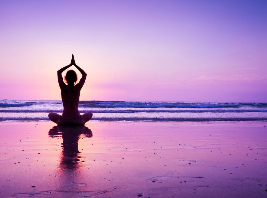 Silhouette of a person meditating in a seated yoga pose on a sunset beach.
