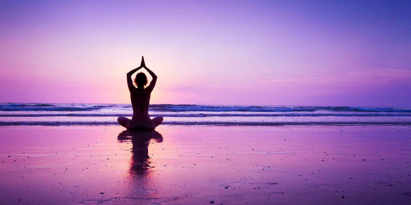 Silhouette of a person meditating in a seated yoga pose on a sunset beach.