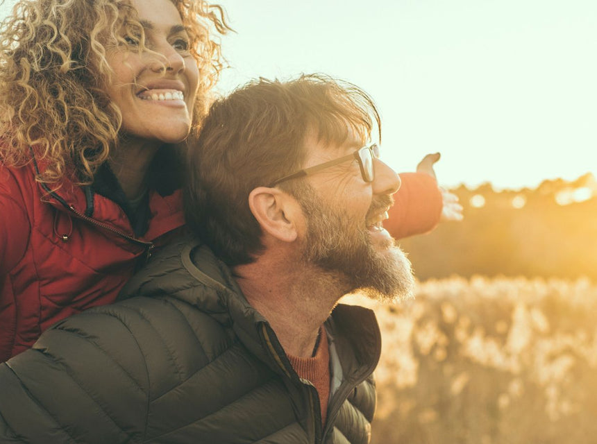 Couple enjoying sunset outdoors, the woman on the man's back smiling.