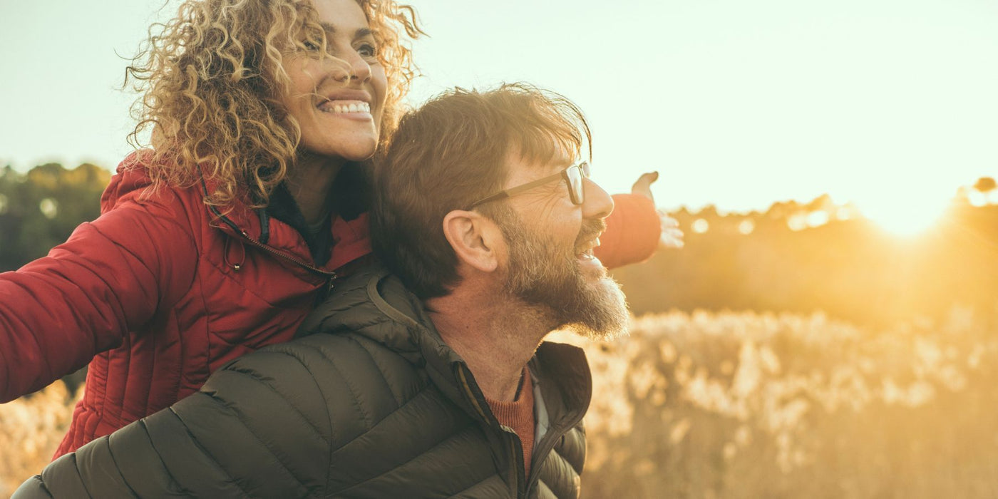 Couple enjoying sunset outdoors, the woman on the man's back smiling.