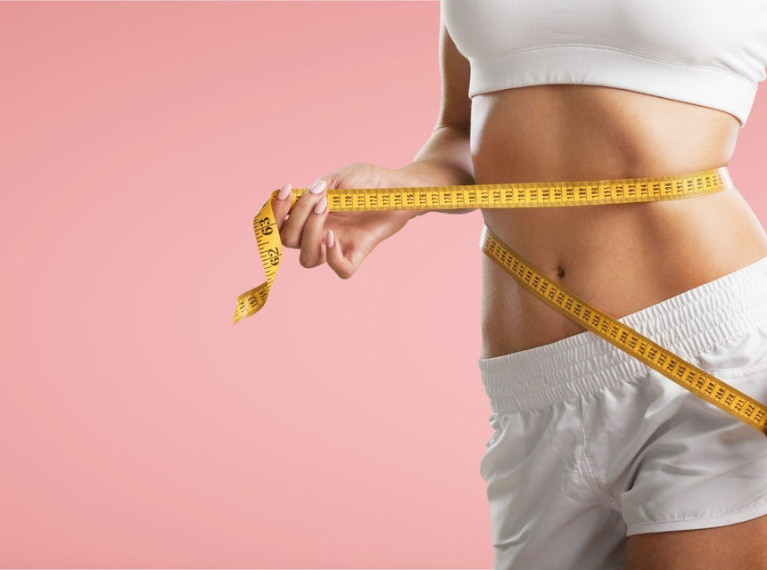 Woman measuring her waist with a yellow tape measure against a pink background