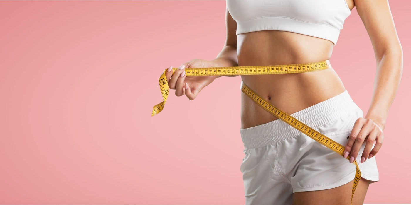 Woman measuring her waist with a yellow tape measure against a pink background