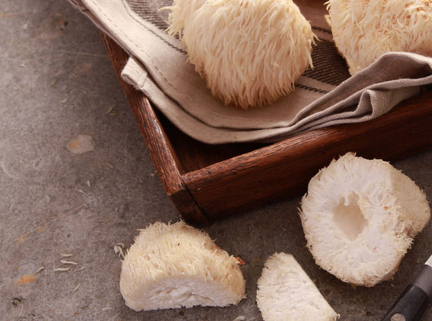 Lions mane mushrooms on a wooden cutting board with a knife nearby