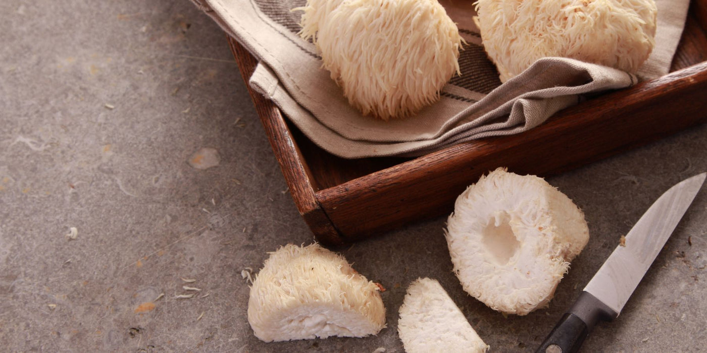 Lions mane mushrooms on a wooden cutting board with a knife nearby