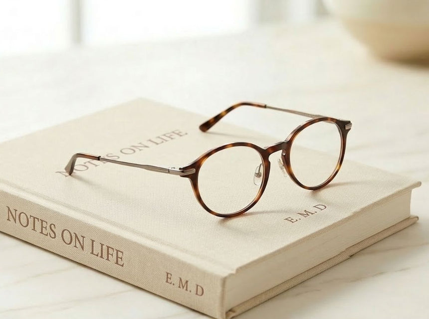 Round tortoiseshell glasses rest on a beige book on a marble surface