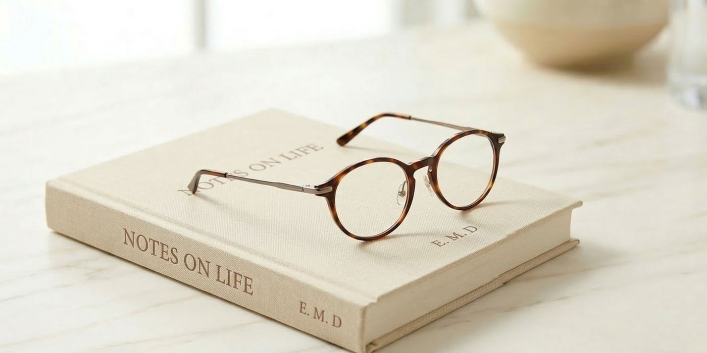 Round tortoiseshell glasses rest on a beige book on a marble surface