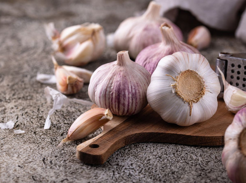Garlic bulbs and peeled cloves arranged on a wooden board with a metal grater in a rustic kitchen setting