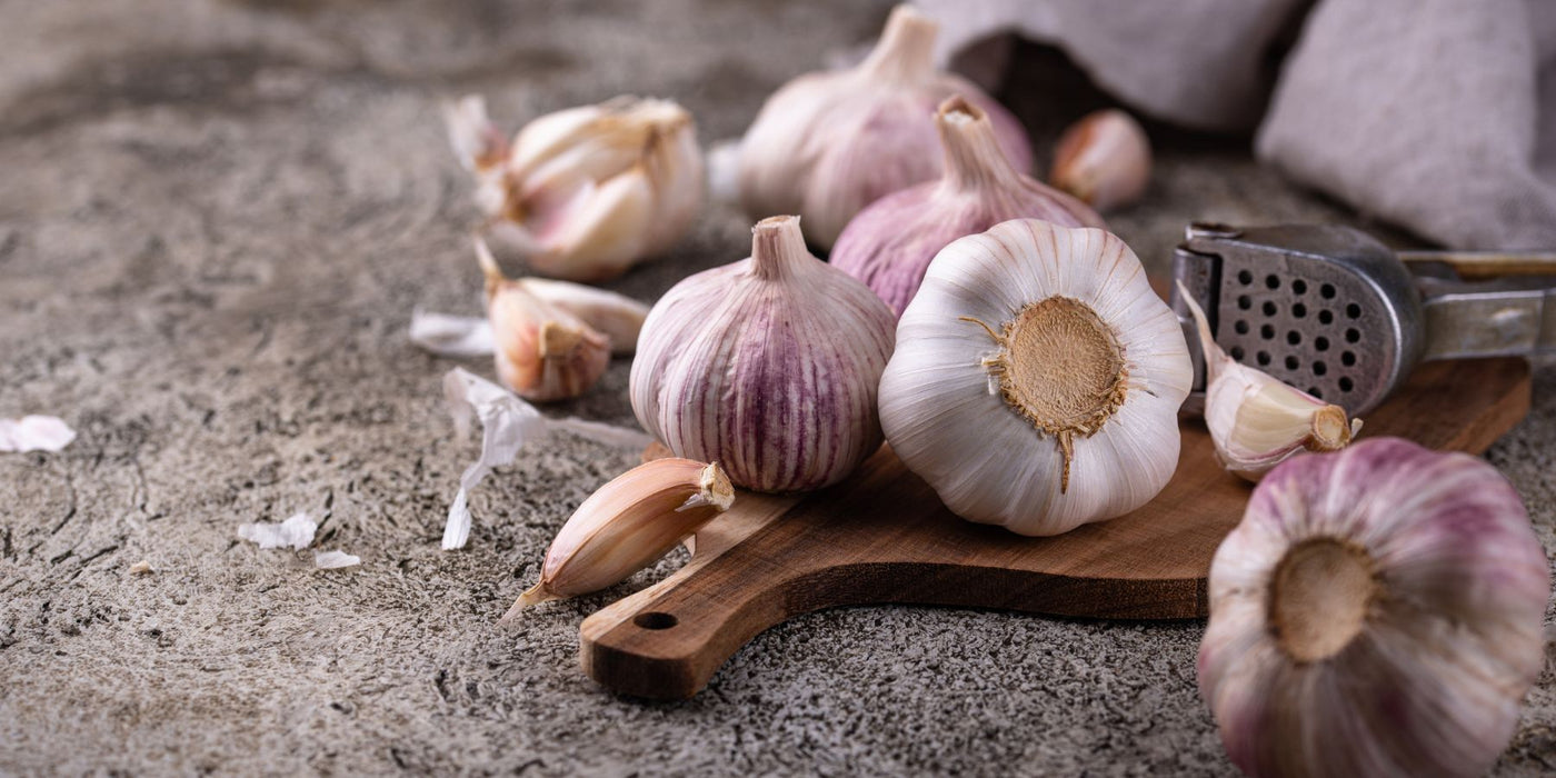 Garlic bulbs and peeled cloves arranged on a wooden board with a metal grater in a rustic kitchen setting