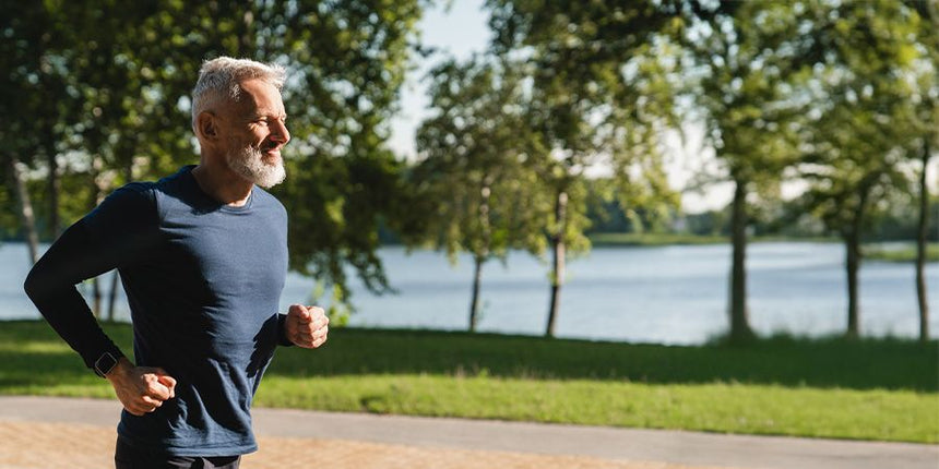 Older man jogging along a park path beside a lake.