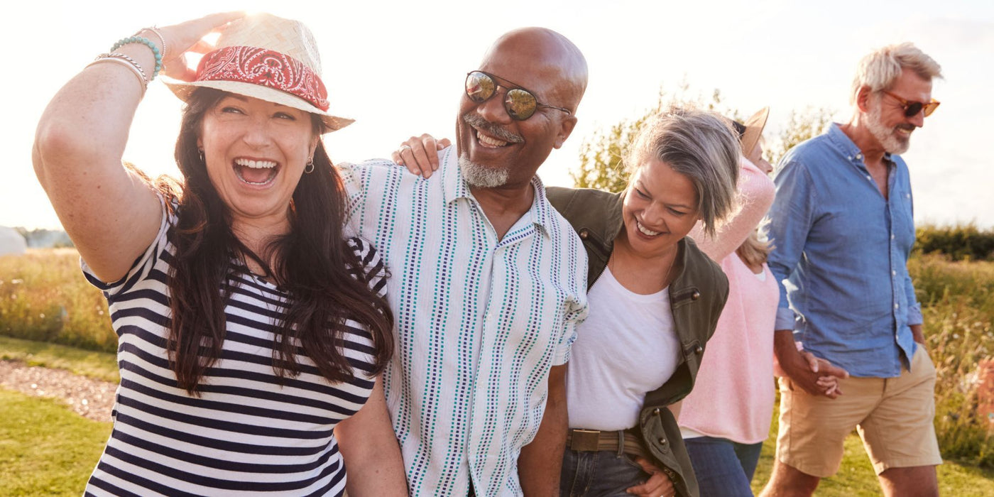 Smiling diverse group of adults walking outdoors in a sunny field representing healthy ageing.