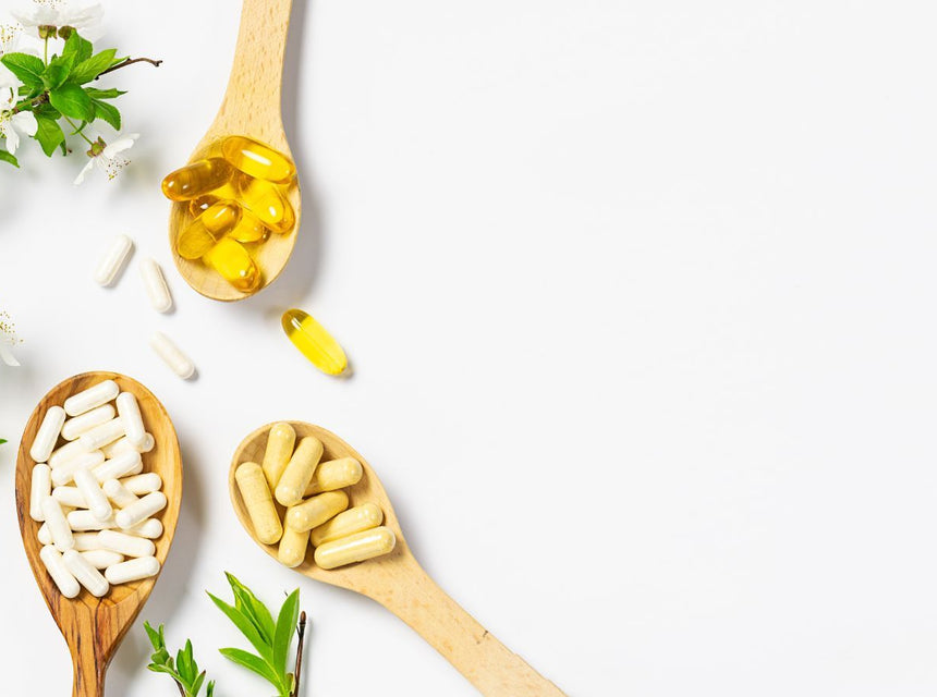 Flat lay of immune support items with capsules, oil and sprigs of blossoms and leaves on white background.
