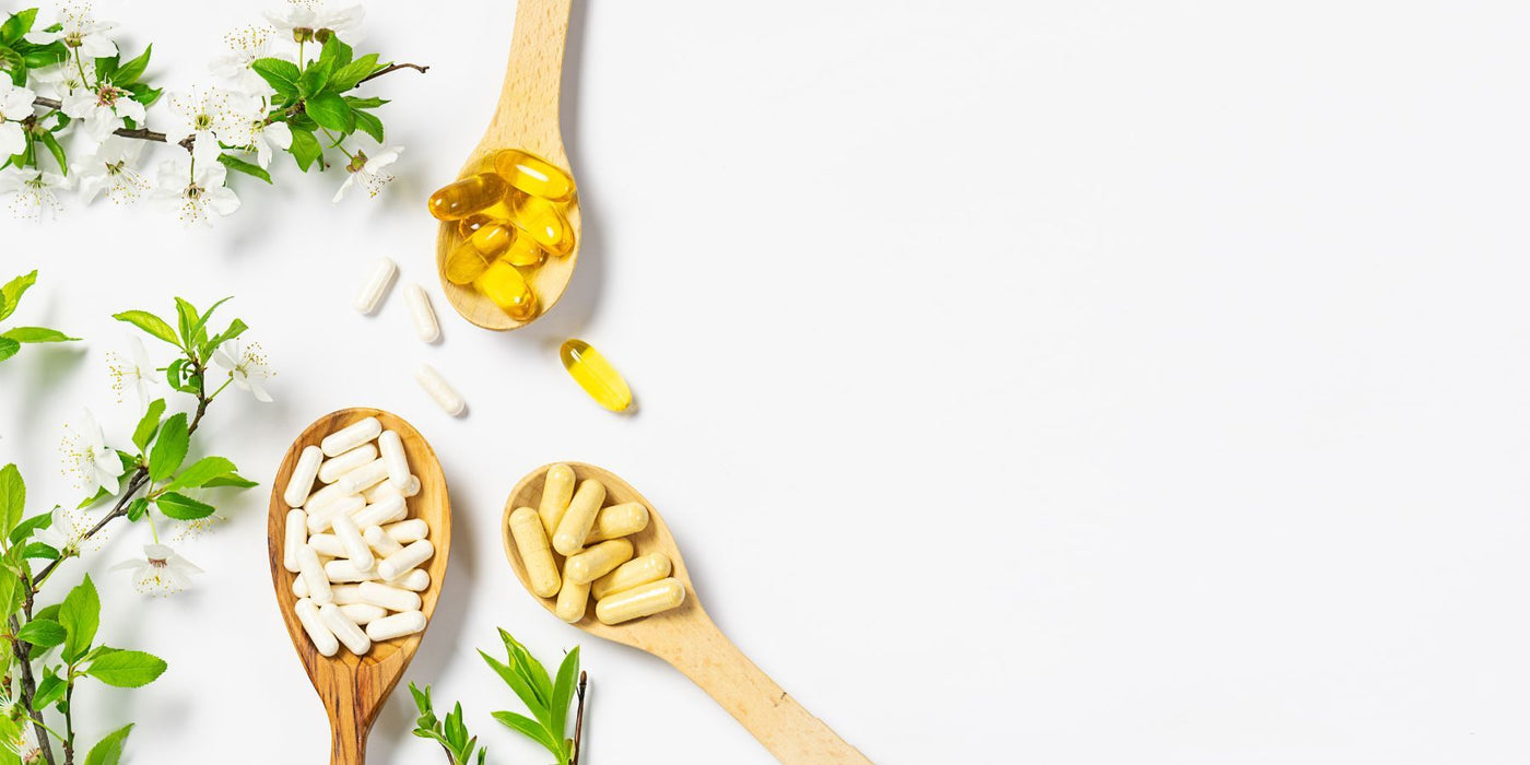 Flat lay of immune support items with capsules, oil and sprigs of blossoms and leaves on white background.