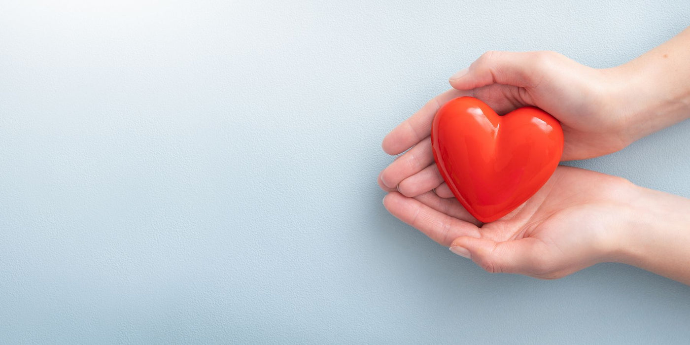Hands cradle a red heart against a pale blue textured background