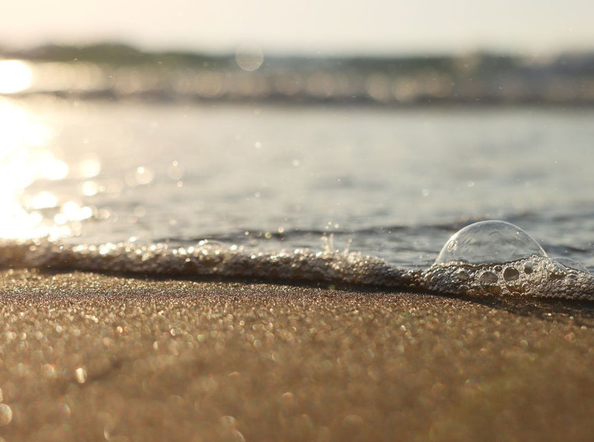 Sunlit shoreline with foamy waves and a single bubble resting on wet sand