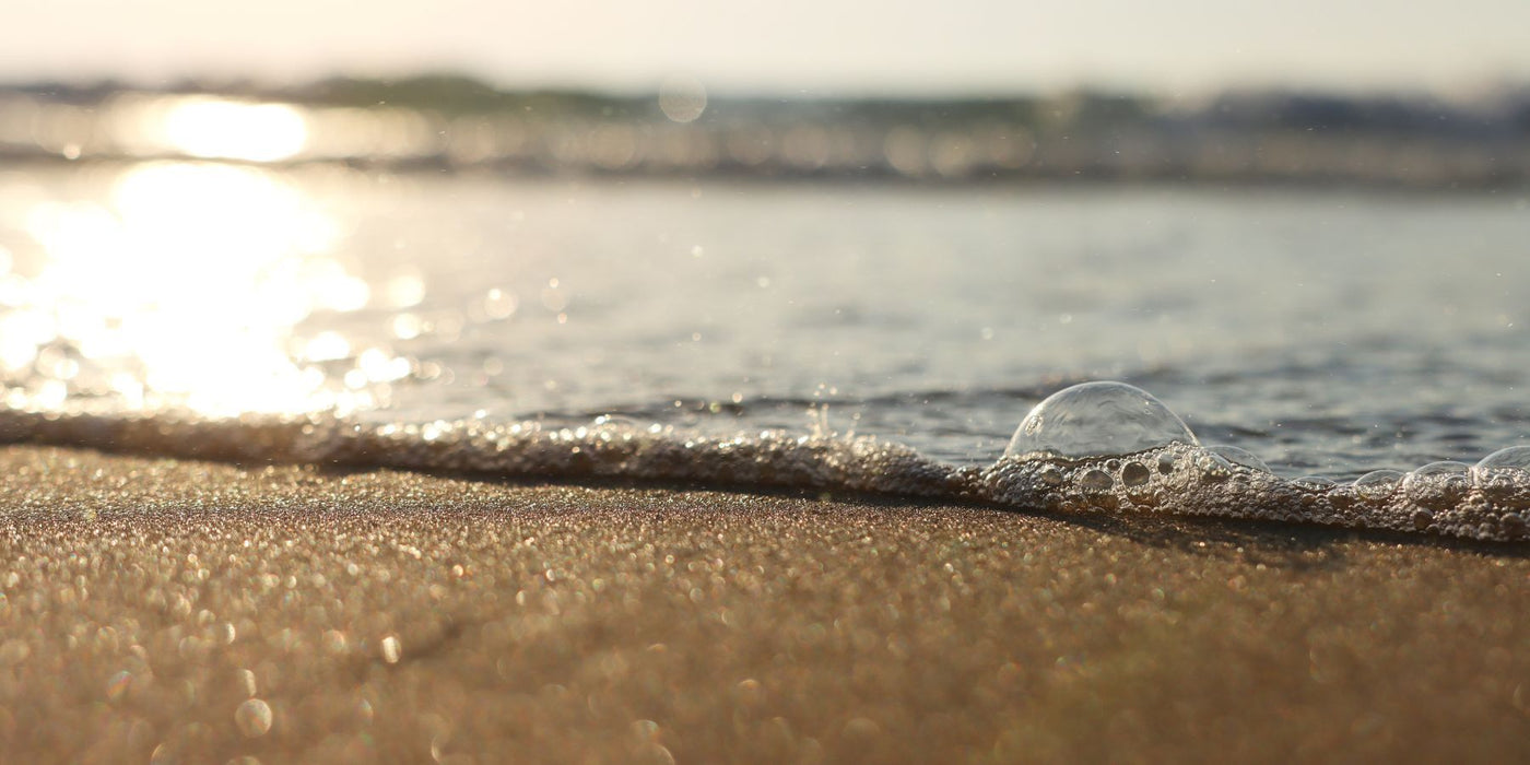 Sunlit shoreline with foamy waves and a single bubble resting on wet sand