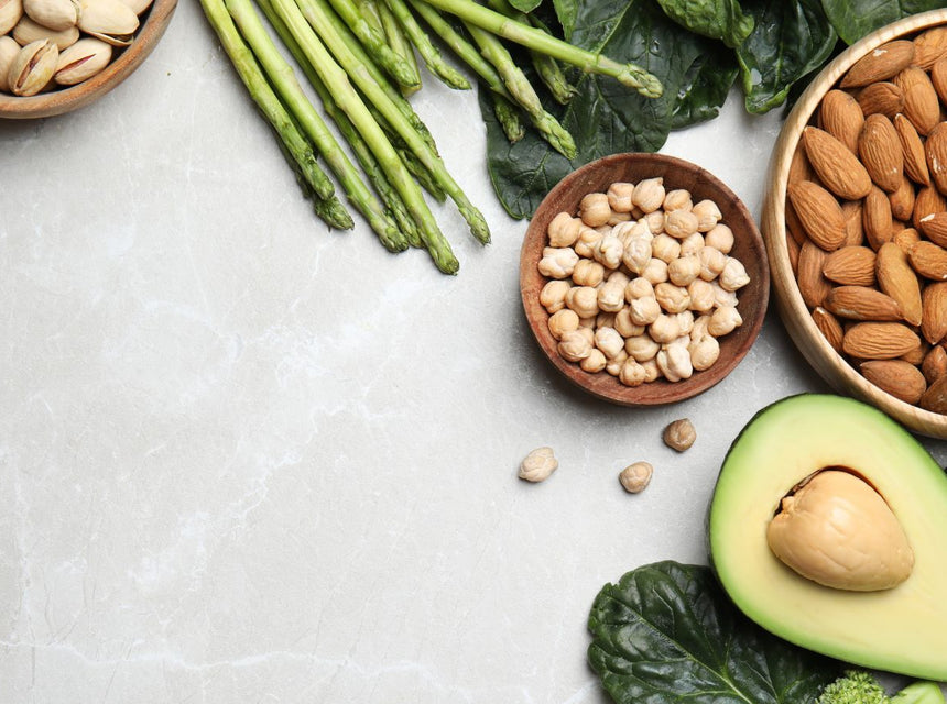 Assorted vitamin E rich foods including almonds pistachios avocado and leafy greens on a marble surface.