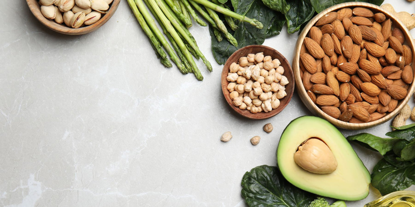Assorted vitamin E rich foods including almonds pistachios avocado and leafy greens on a marble surface.