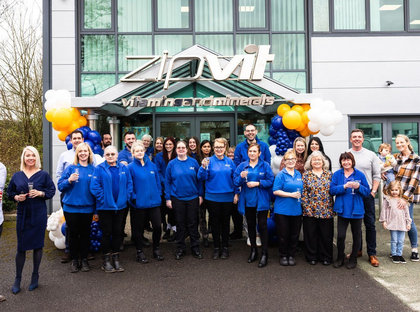 Zipvit team outside a modern building posing for a group photo in blue jackets with balloons.