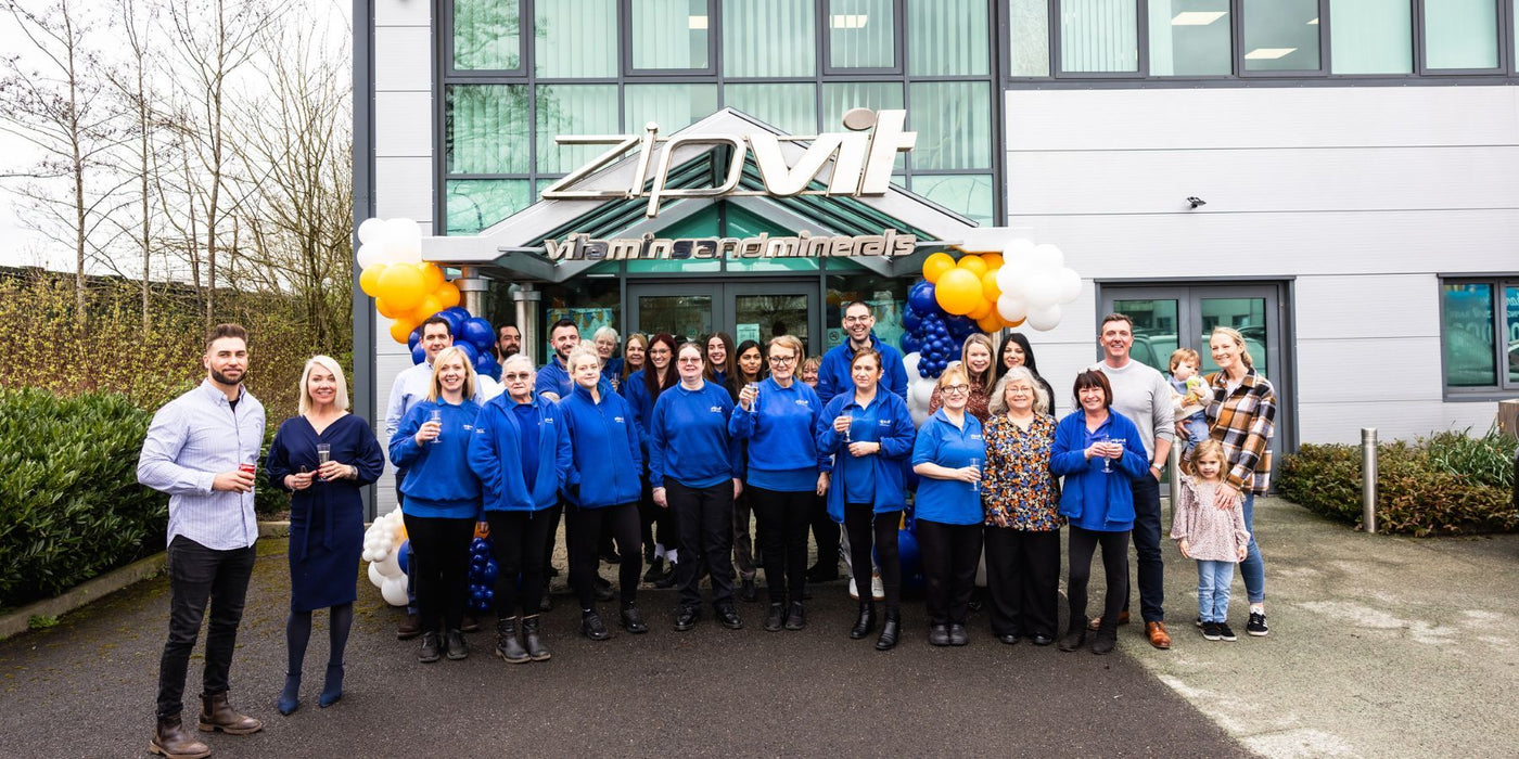 Zipvit team outside a modern building posing for a group photo in blue jackets with balloons.