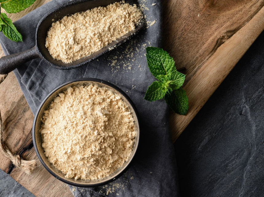 Powder maca on a wooden board with a scoop and fresh mint leaves
