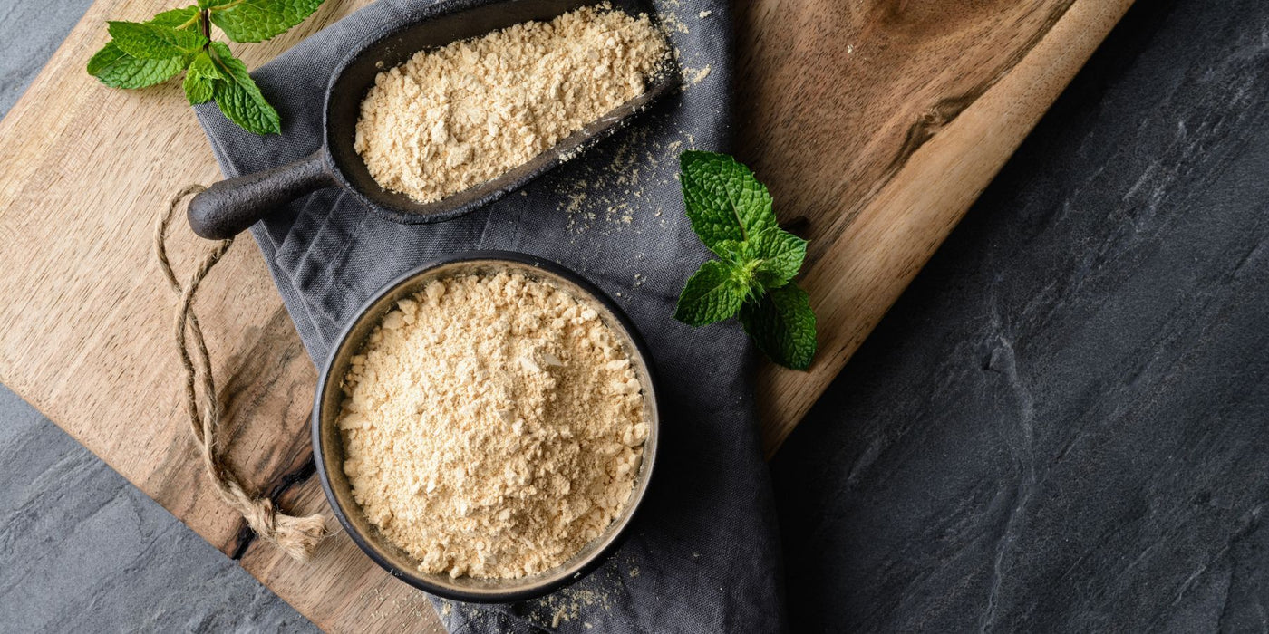Powder maca on a wooden board with a scoop and fresh mint leaves