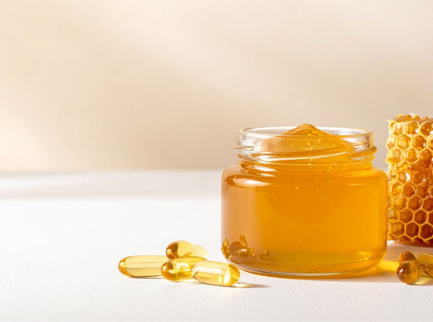 Jar of honey with a honeycomb and several capsules on a light surface.