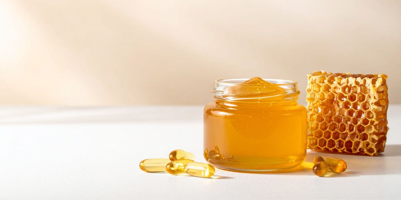 Jar of honey with a honeycomb and several capsules on a light surface.