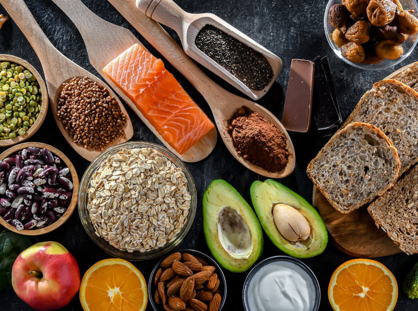 Assorted healthy foods on a dark surface including bananas salmon avocado oats bread beans and fruit
