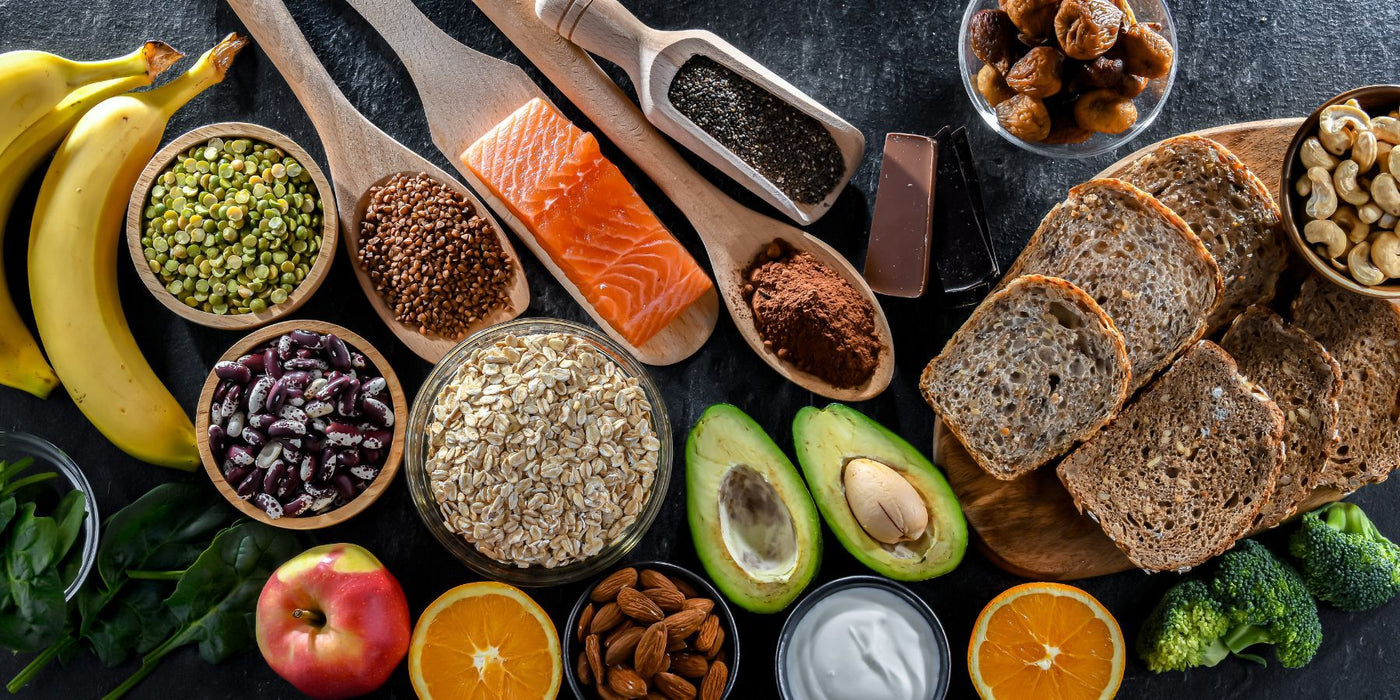 Assorted healthy foods on a dark surface including bananas salmon avocado oats bread beans and fruit