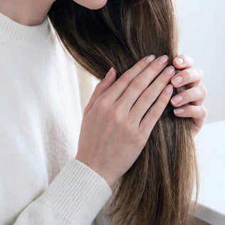Hands with a neat manicure hold long hair, highlighting hair health.