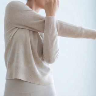 Person in a cream knit sweater stretches an arm in a bright, airy room.