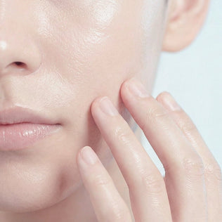 Close-up of a woman's dewy skin as fingers touch her cheek for collagen skincare.