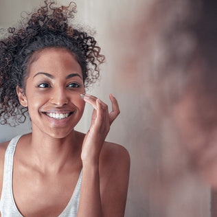Smiling woman with curly hair applies skincare cream to her face