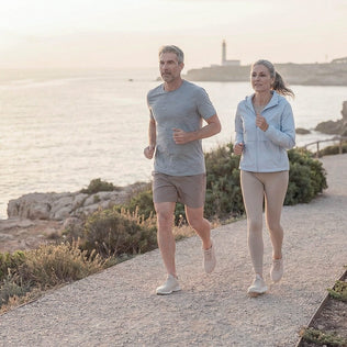 Couple jogging along a coastal path at sunset with a lighthouse in the distance