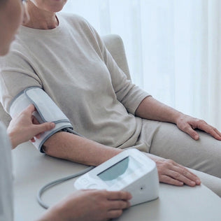 Older adult seated as a clinician checks blood pressure with a digital cuff and monitor