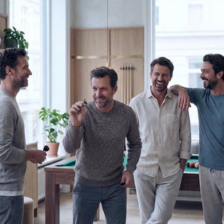 Group of men in casual knitwear laugh together in a modern indoor space near a pool table.