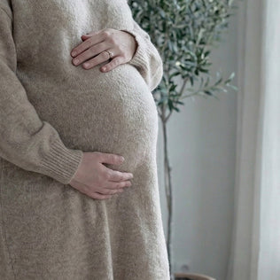 Pregnant woman in a beige knitted sweater gently cradles her baby bump