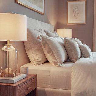 Cozy neutral bedroom featuring a plush bed with beige pillows and warm glass lamps on wooden nightstands.