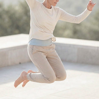 Person in cream clothing jumps mid air on an outdoor terrace with a sunny background.