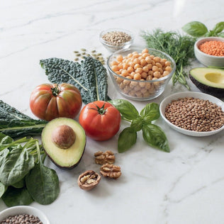 Vibrant vegan spread with tomatoes avocado leafy greens lentils chickpeas and herbs on a marble countertop.