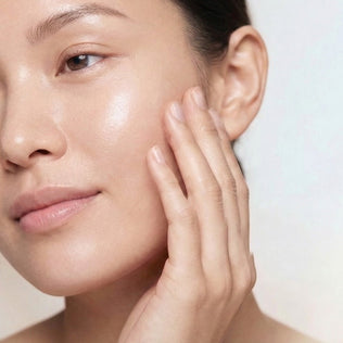 Close up of a woman's face with dewy skin touching her cheek